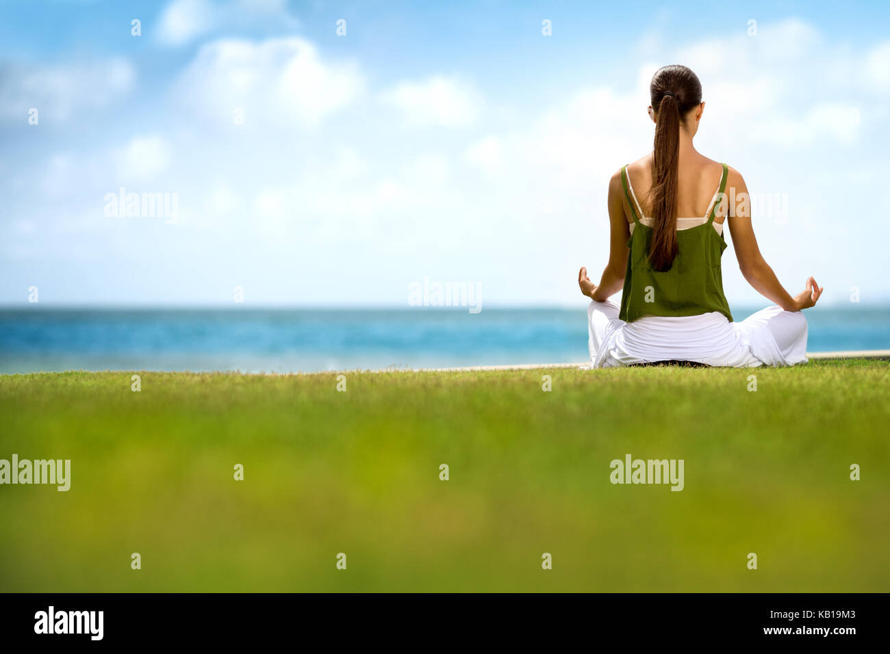 Woman sitting on grass and doing yoga near the ocean Stock Photo - Alamy