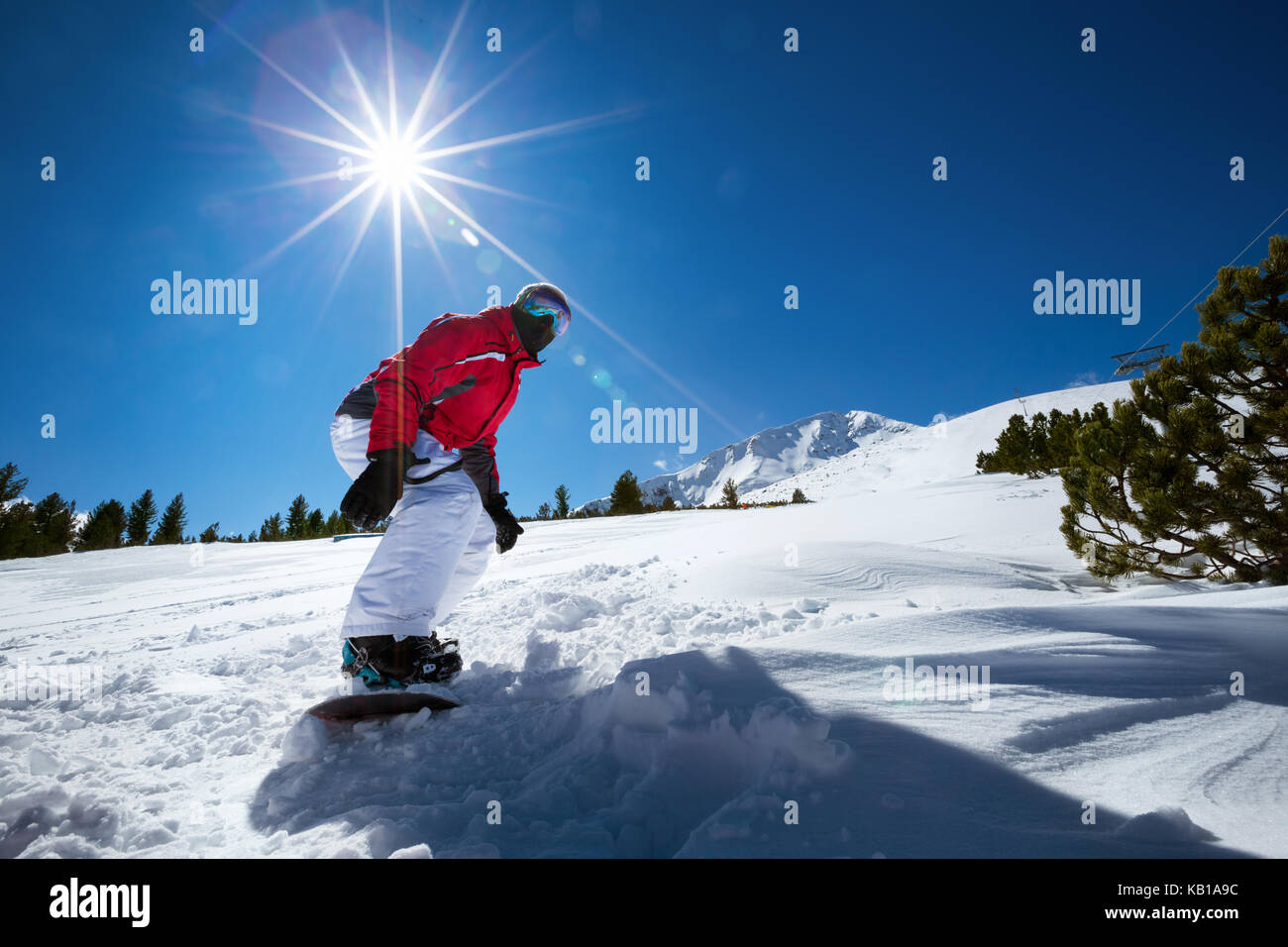 Snowboarder slides down snowy ski slope on snowboard. Stock Photo