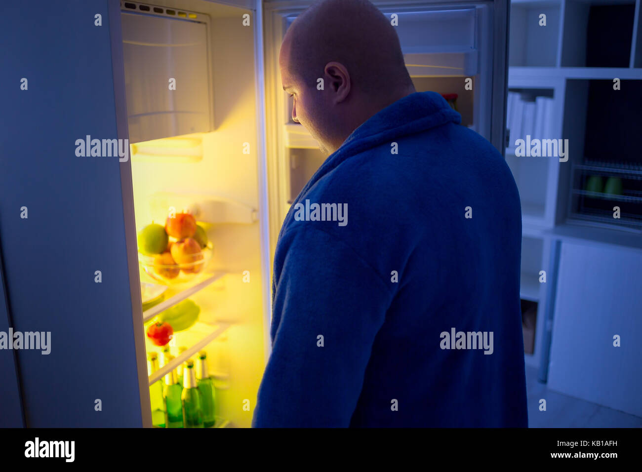 overweight guy at night open refrigerator looking for food Stock Photo