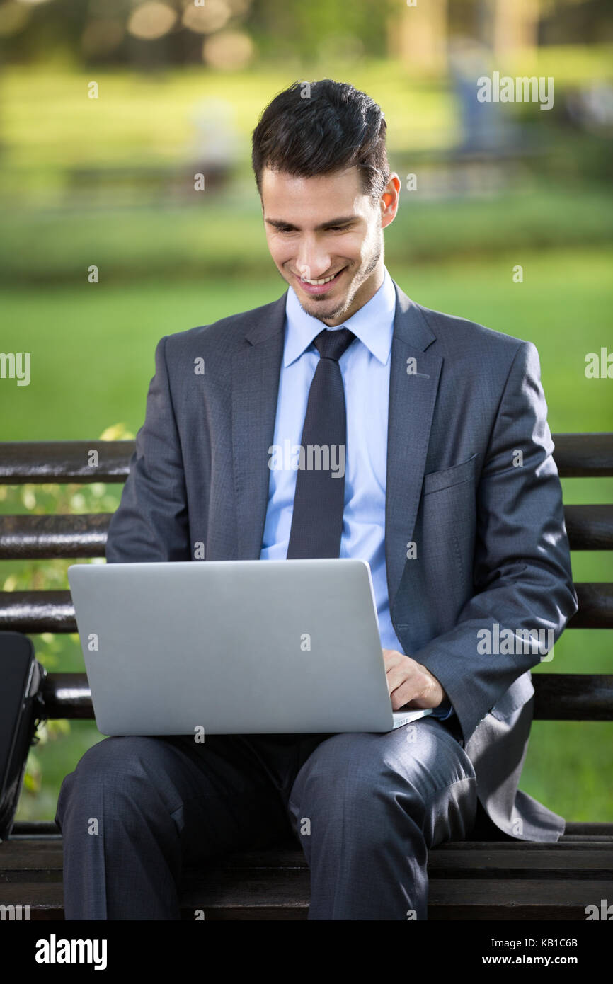 Businessman sitting on bench with laptop in park Stock Photo - Alamy