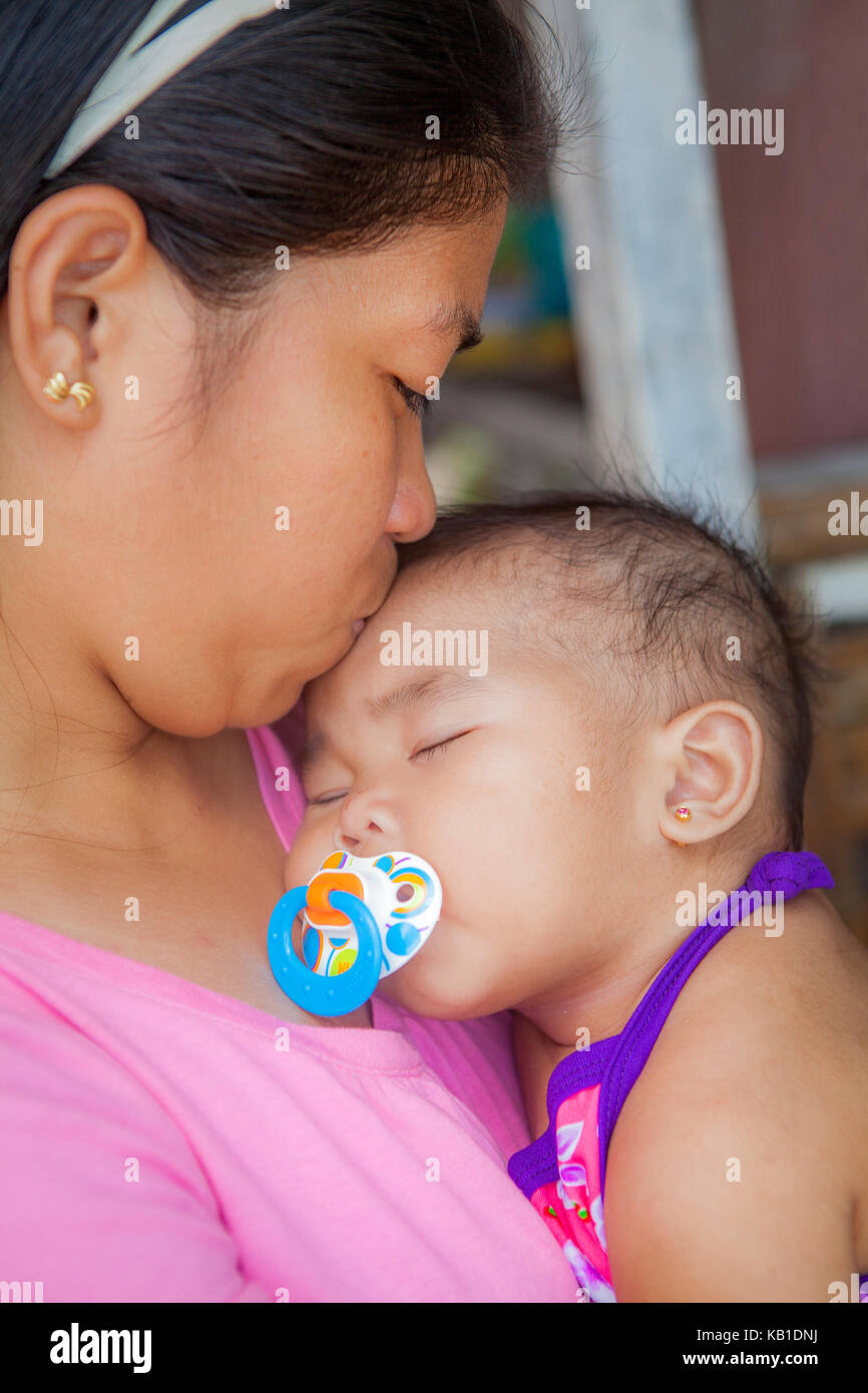 Tender moment as a Filipino mother kisses her sleeping baby on her head while the baby sucks on her binky. Stock Photo
