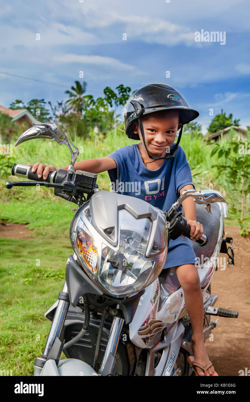 A four-year old Filipino boy sits on a motorcycle pretending to ride it in Ormoc City, Leyte Island, Philippines. Stock Photo