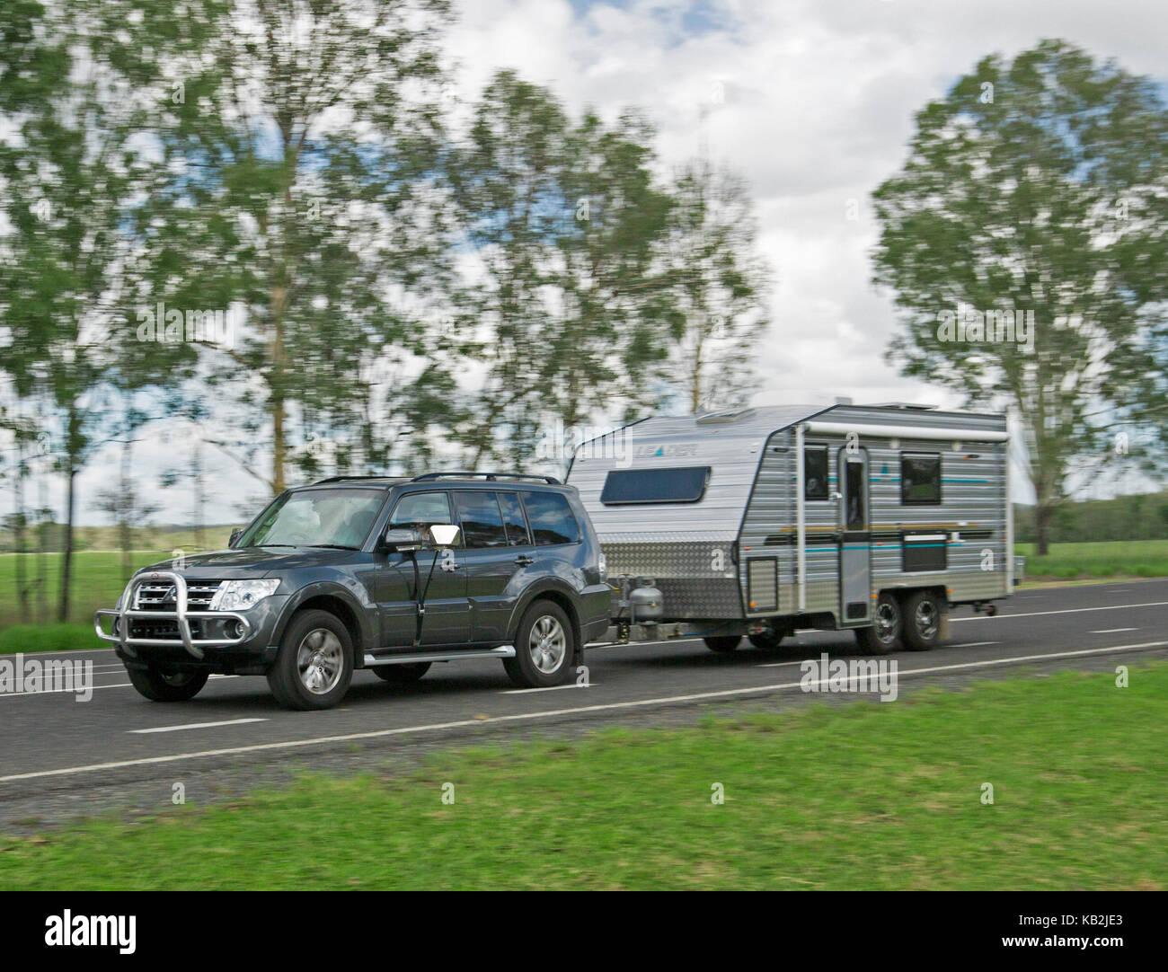 Dark grey four wheel drive vehicle towing caravan along bitumen road