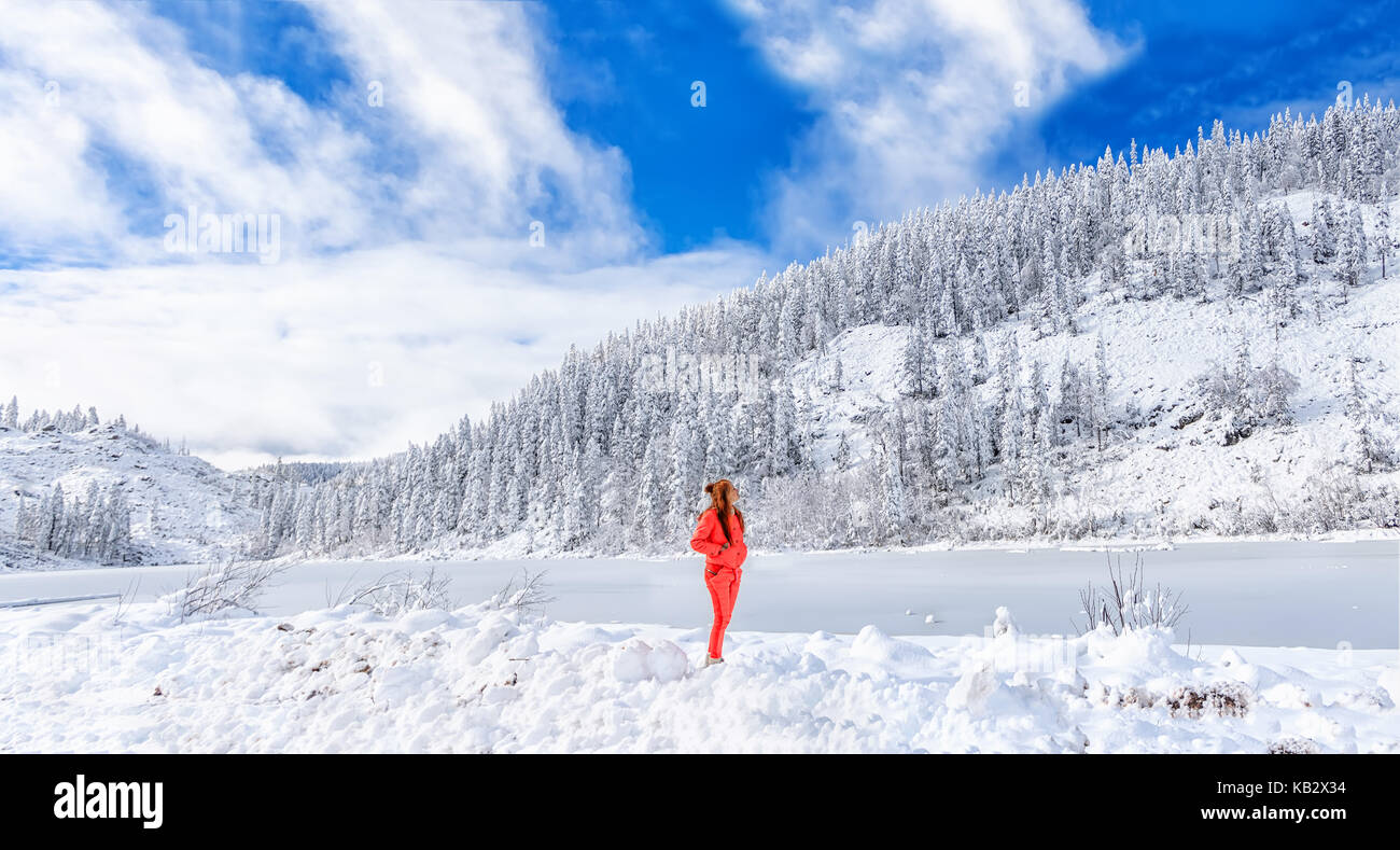 A young girl admires the winter landscape on the lake. Beautiful lake Amut in taiga hills on Far East of Russia in early october. Mountain lake in win Stock Photo
