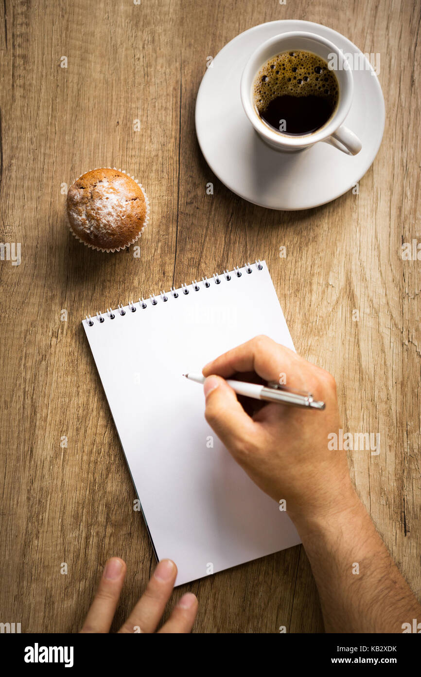 Man’s hand writing on paper with cup of coffee on wooden table, top view. Stock Photo