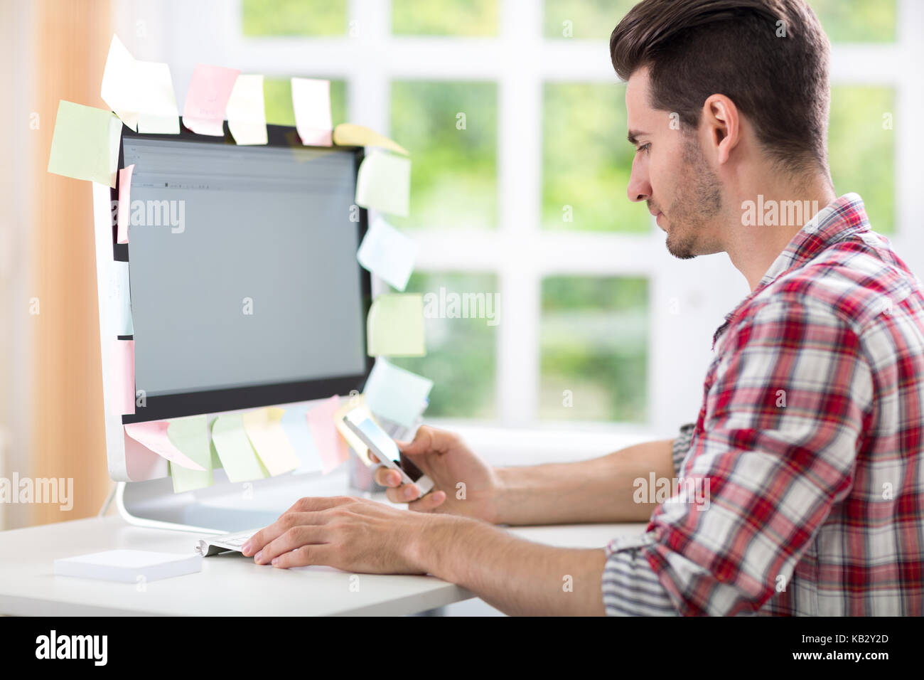 overworked man typing on computer with stickers on monitor Stock Photo
