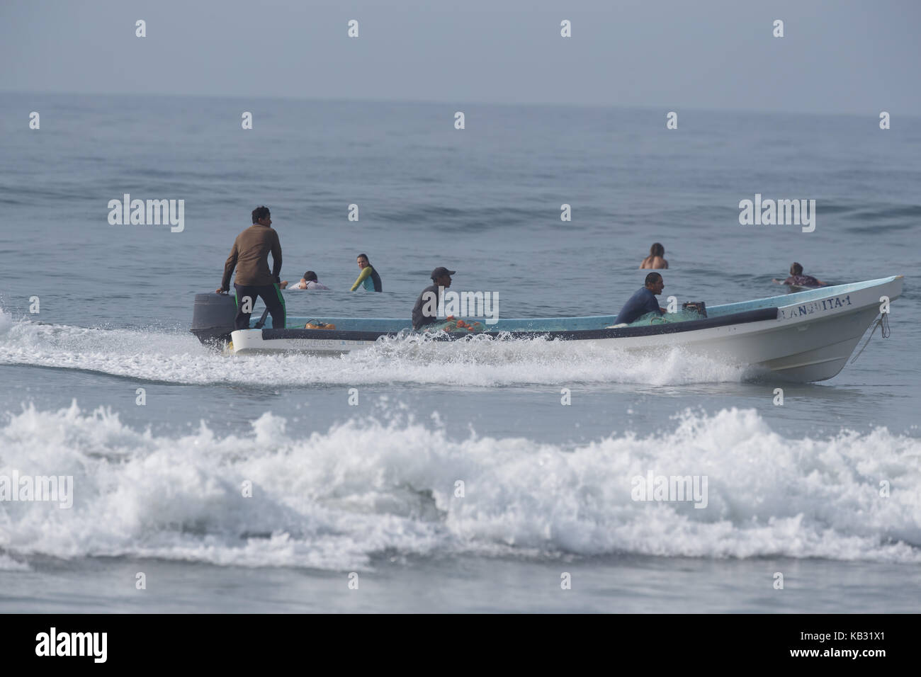 Fisherman in a panga steer past surfers at La Bamba beach near Salina Cruz, Oaxaca, Mexico. Stock Photo