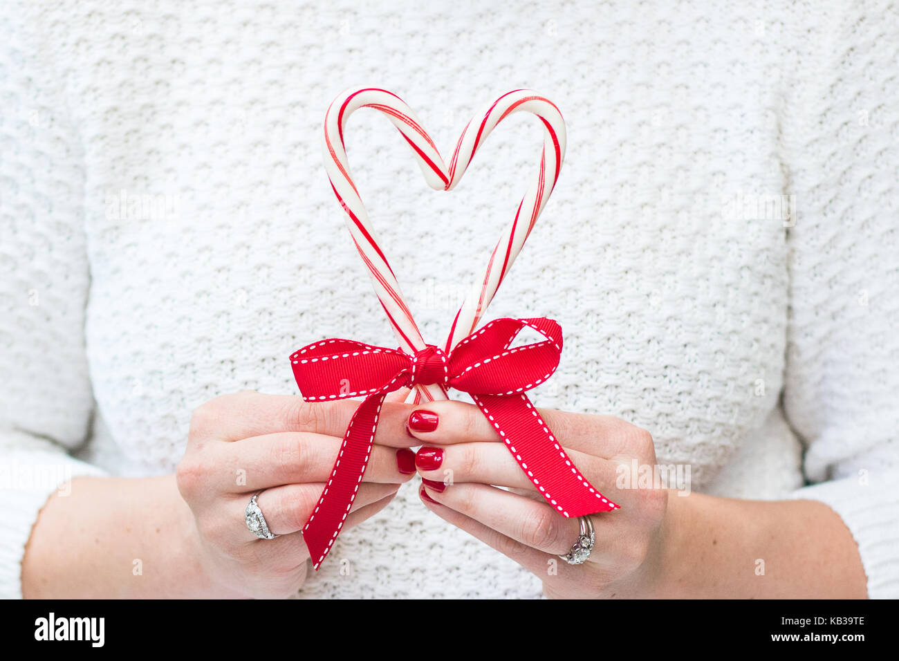 Woman holding Merry Christmas Candy Canes and a red bow in a white sweater in front of a rustic background with room for copy Stock Photo