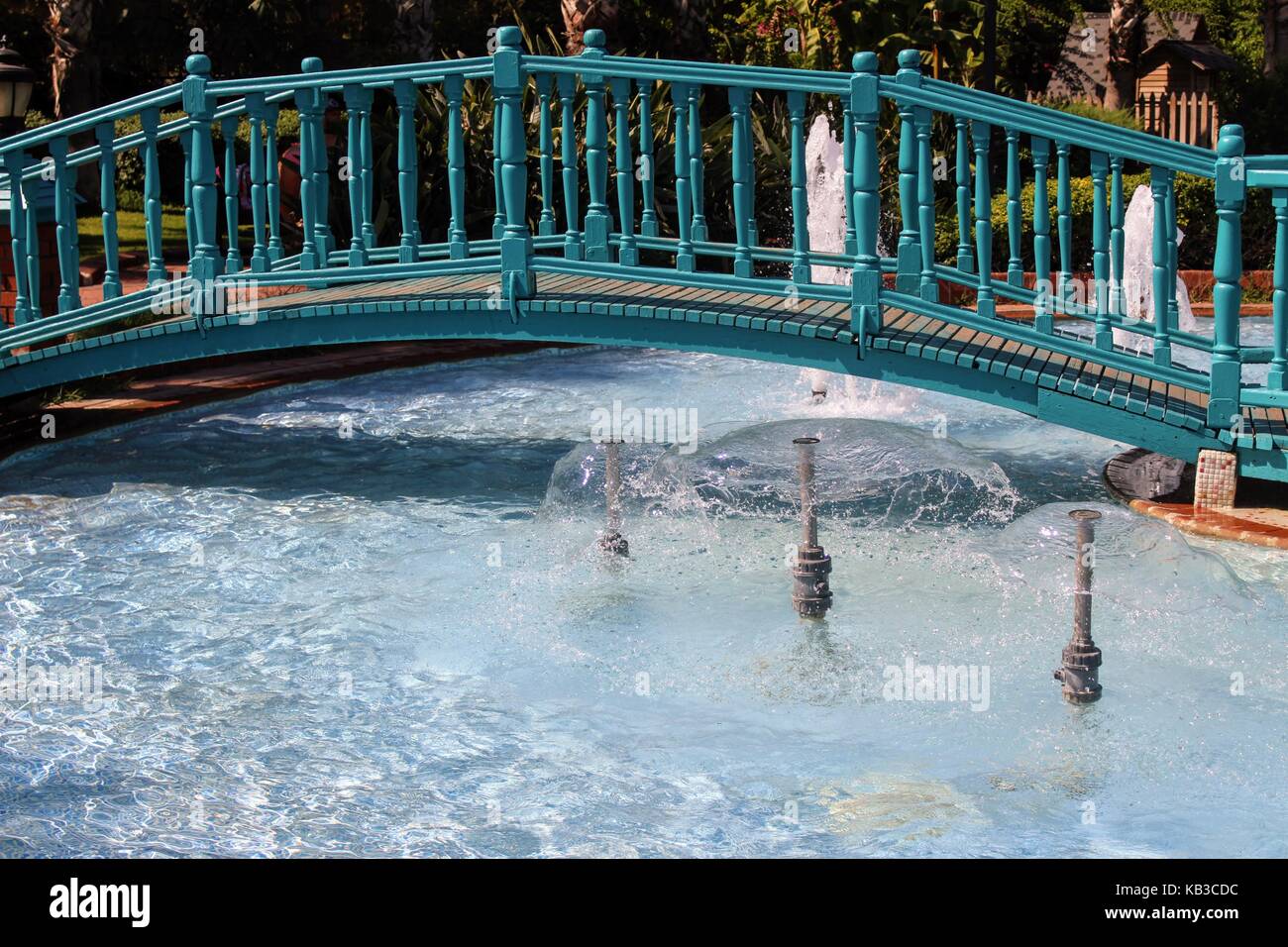 A wooden bridge over the pool with fountains in the park of the 100th