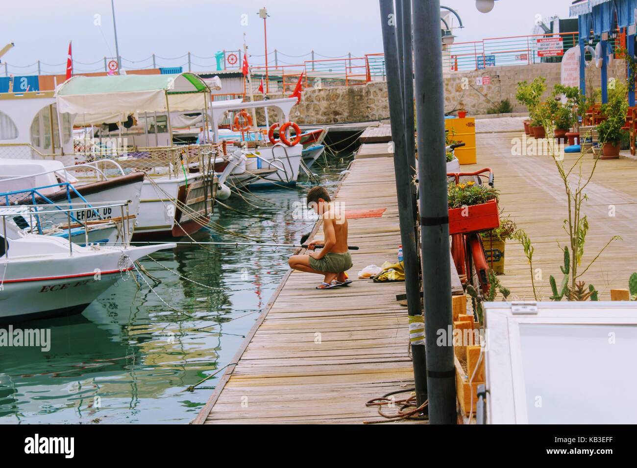 The boy is fishing on a fishing pole from the pier in the city harbor (Antalya, Turkey) in July 2017. Stock Photo