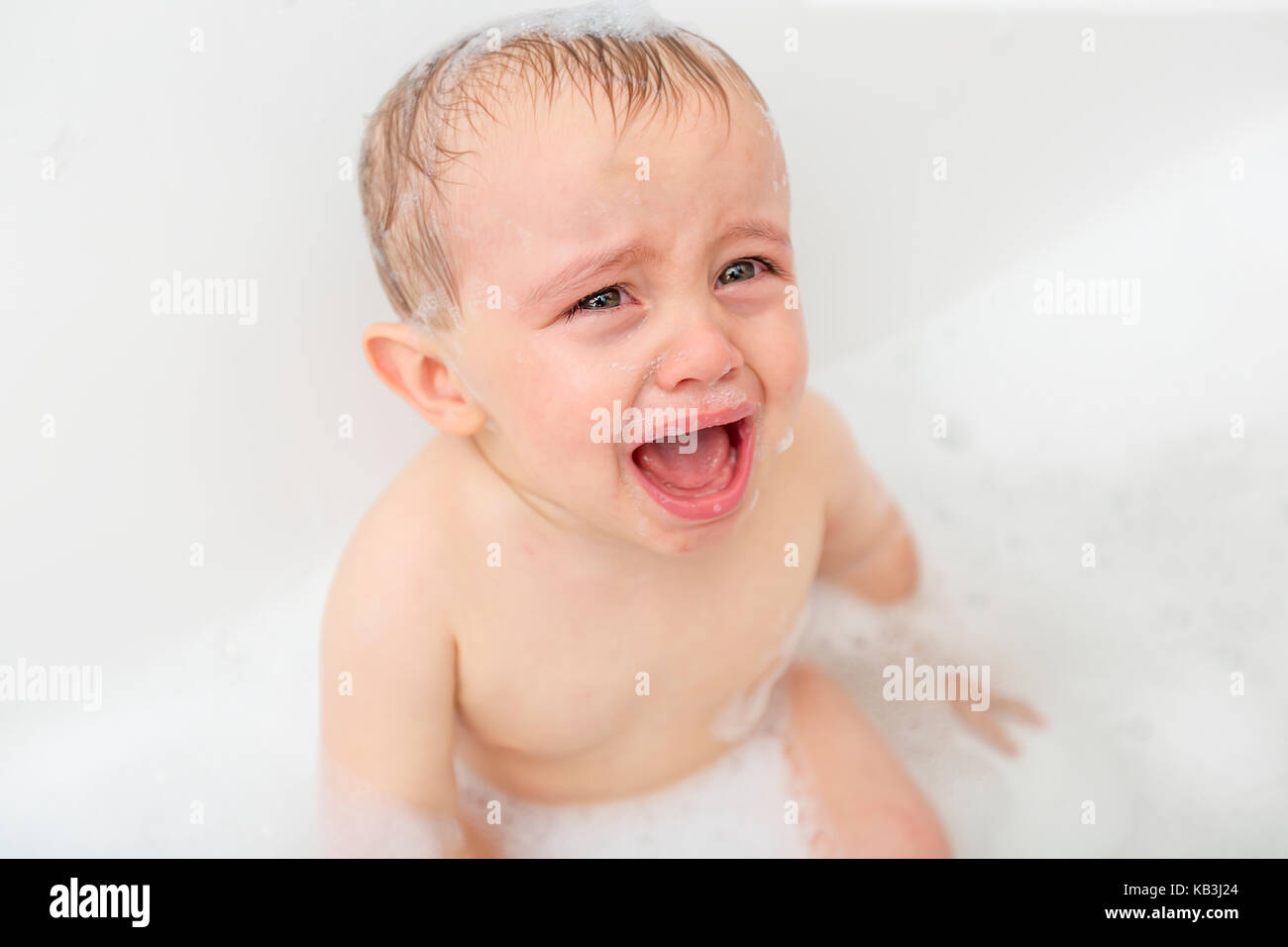 Crying baby by in a bathtub. Infant kid sreaming while taking a bath