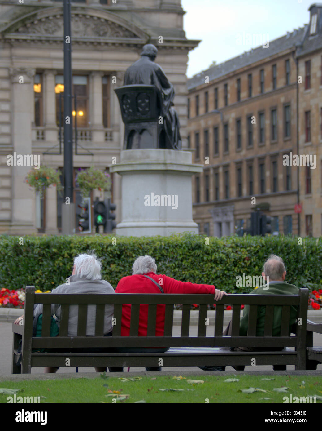 old people  seniors sitting on a bench George square Glasgow mirroring sitting statue Stock Photo