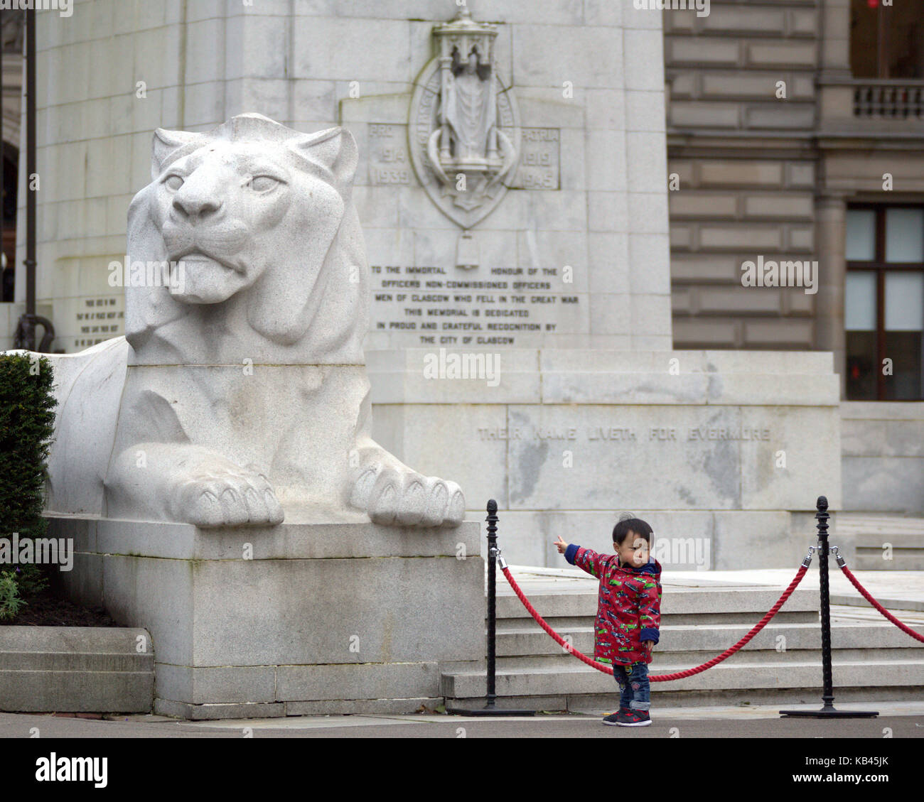 Chinese  kid young boy tourist pointing George square George square cenotaph lion Glasgow Stock Photo