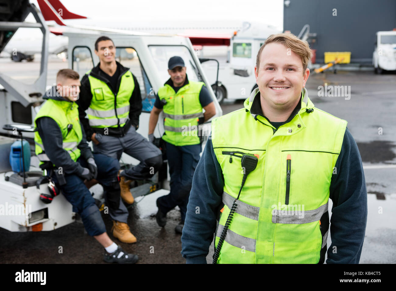 Portrait of confident mid adult male worker smiling while colleagues resting at gangway on runway Stock Photo