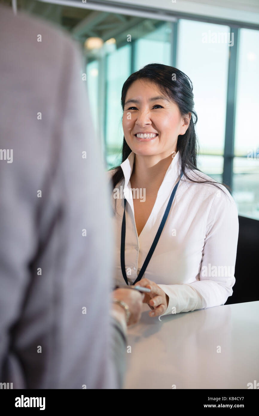 Happy female receptionist looking at businesswoman at counter in airport Stock Photo
