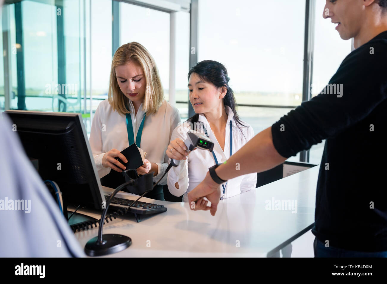 Mid adult receptionist scanning passengers smart watch while colleague checking passport at counter in airport Stock Photo