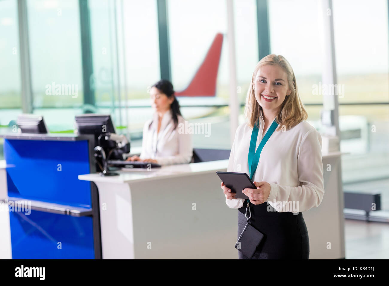 Portrait of young ground staff holding digital tablet while colleague working at reception in airport Stock Photo