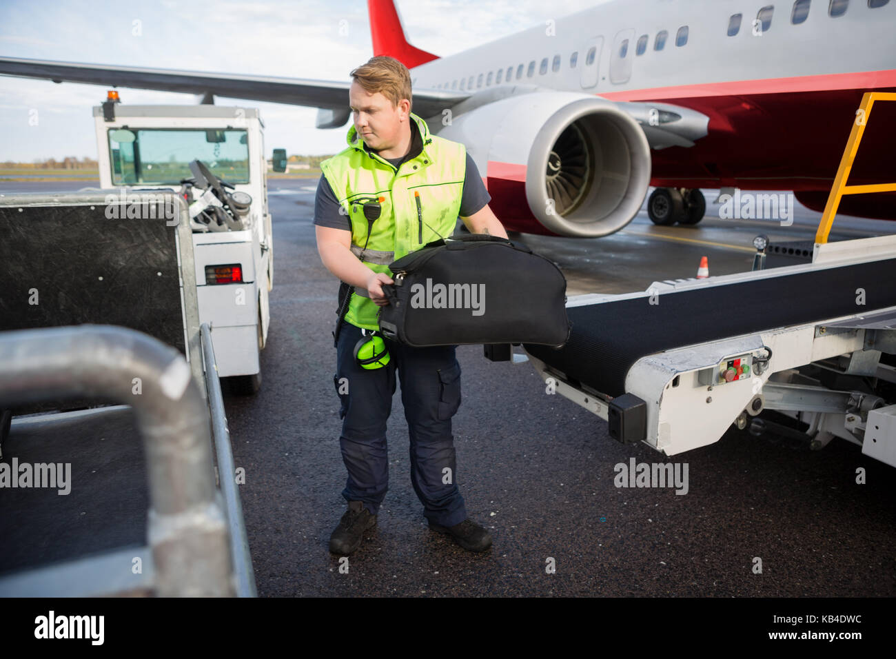 Full length of mid adult worker lifting luggage from conveyor attached