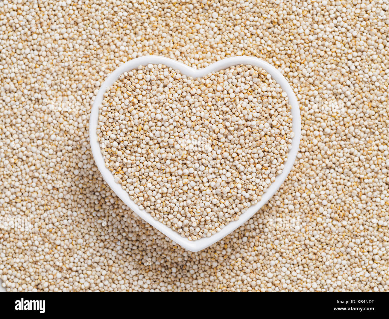 Quinoa in heartshaped bowl on quinoa background. Gluten free ancient