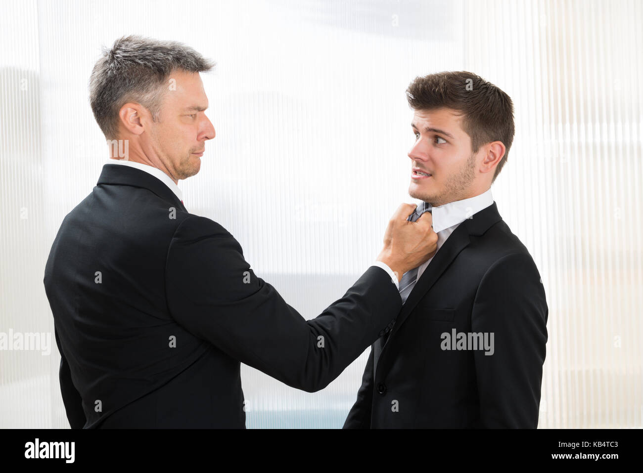 Portrait Of Angry Businessman Holding Young Businessman's Tie In Office Stock Photo