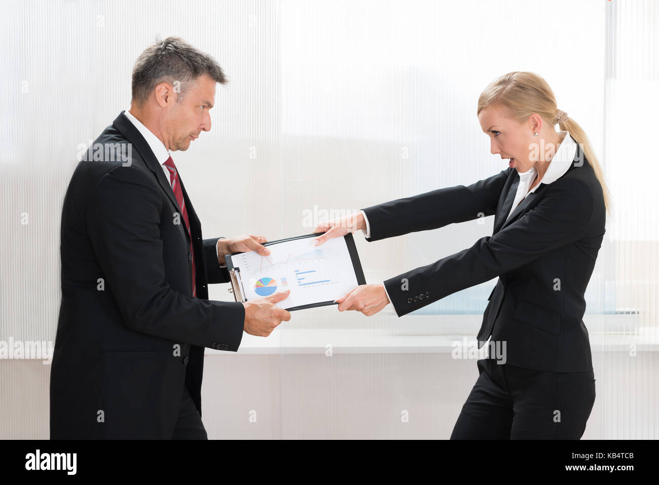 Portrait Of Two Businesspeople Pulling Clipboard With Graph Paper In Office Stock Photo