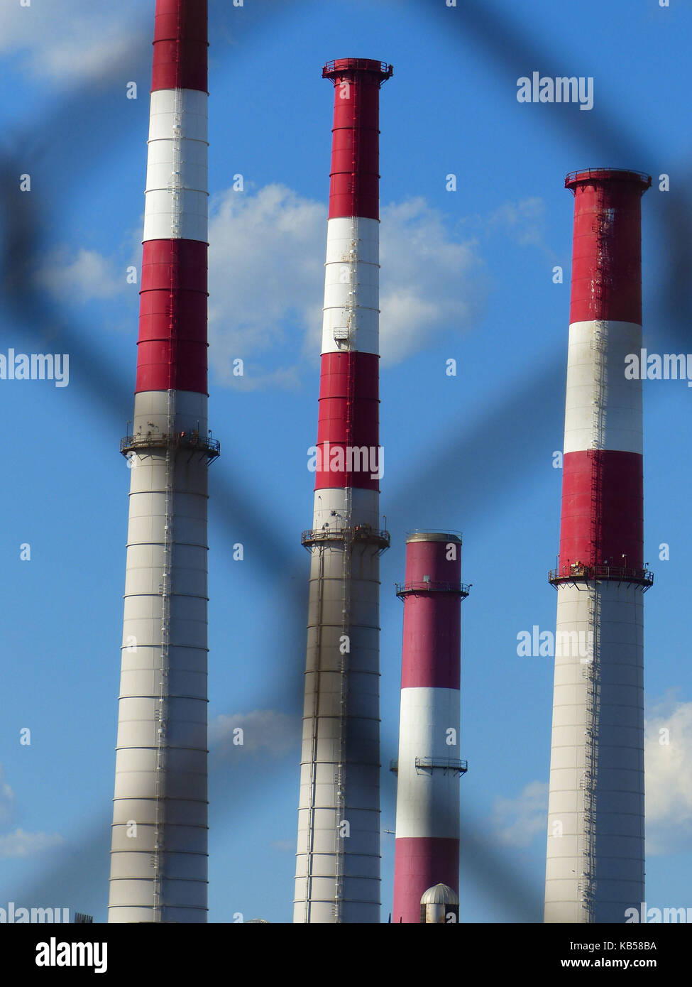 Factory chimneys, photographed through chain linked fence, painted red and white to warn passing aircraft Stock Photo
