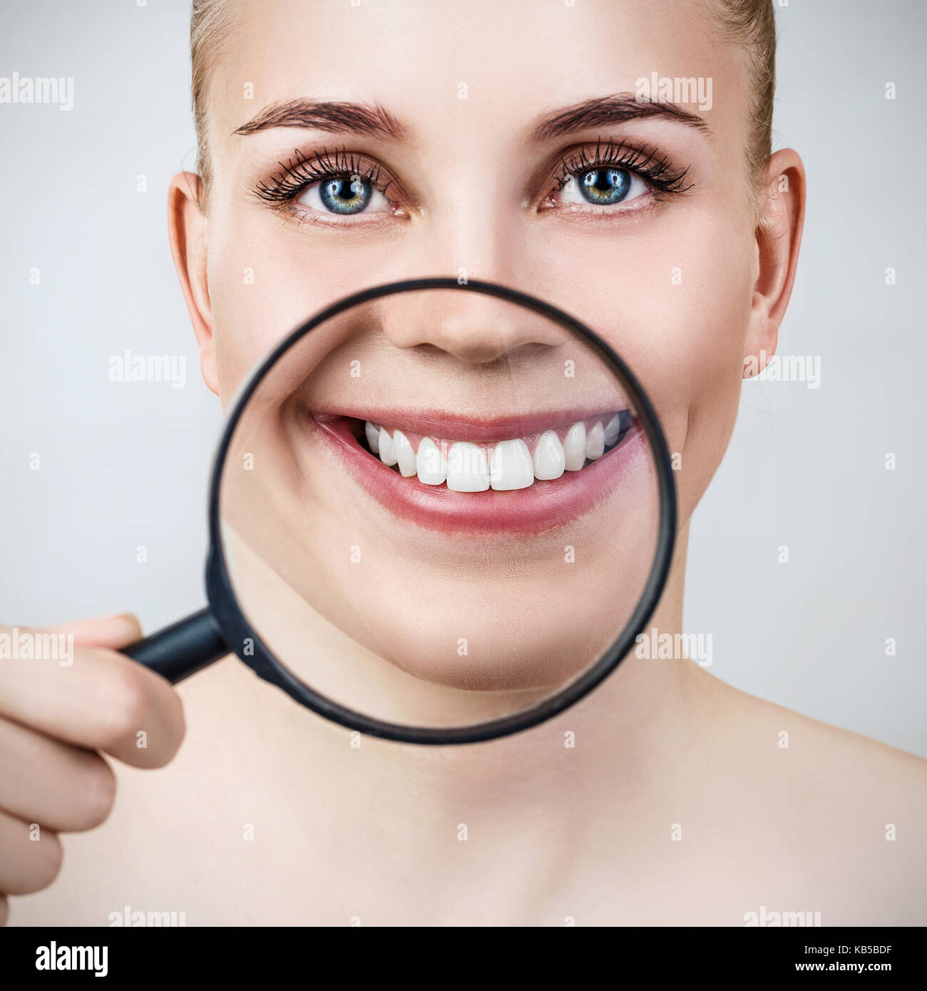 Woman with magnifying glass presents white teeth. Stock Photo