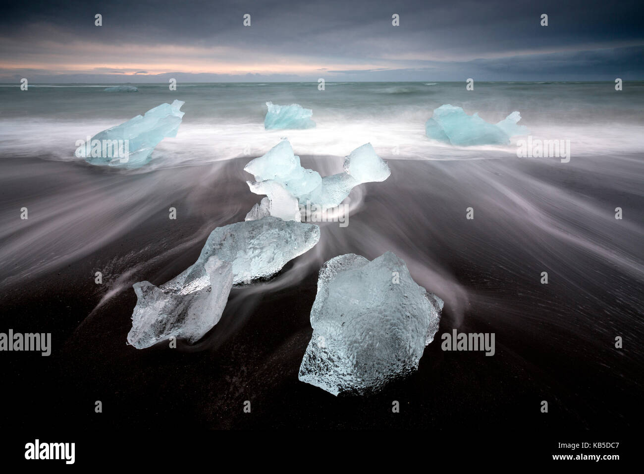 Glassy pieces of ice on volcanic black sand beach with blurred waves ...