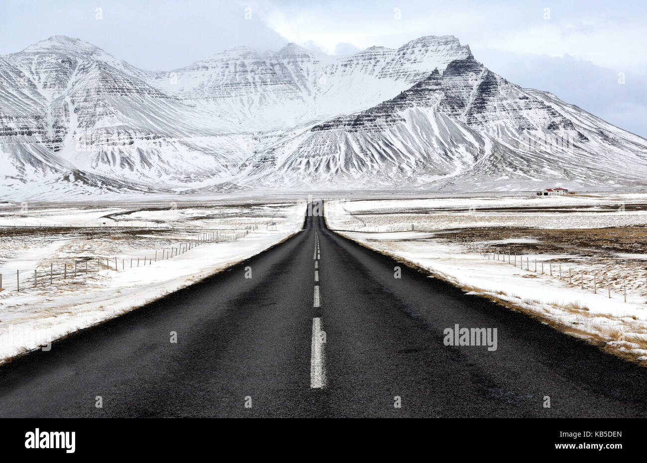 Black tarmac road leading towards snow covered mountains in winter, South Iceland, Polar Regions Stock Photo