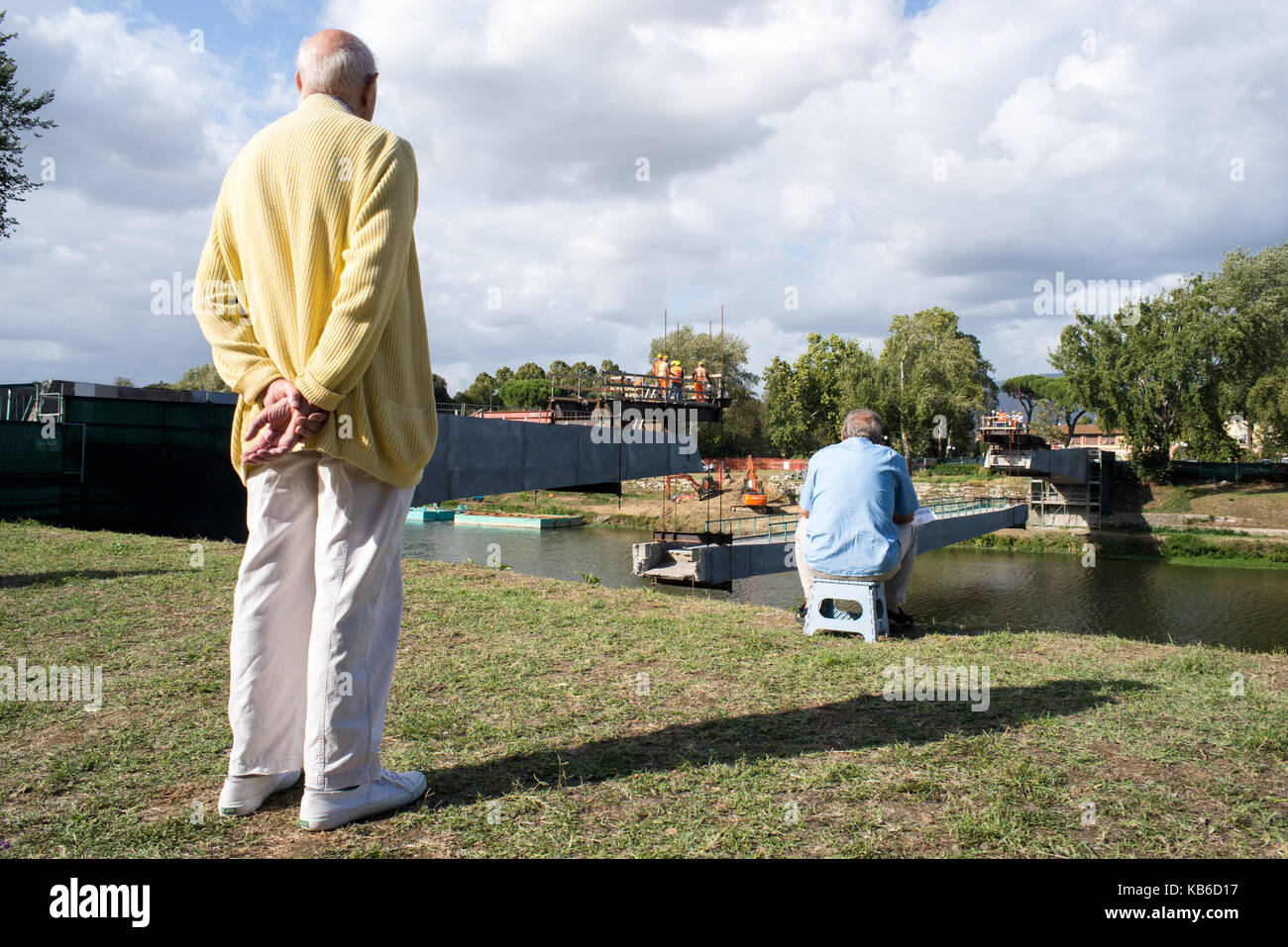 Two elderly men look at the renovation work of a bridge in Florence from a bench Stock Photo
