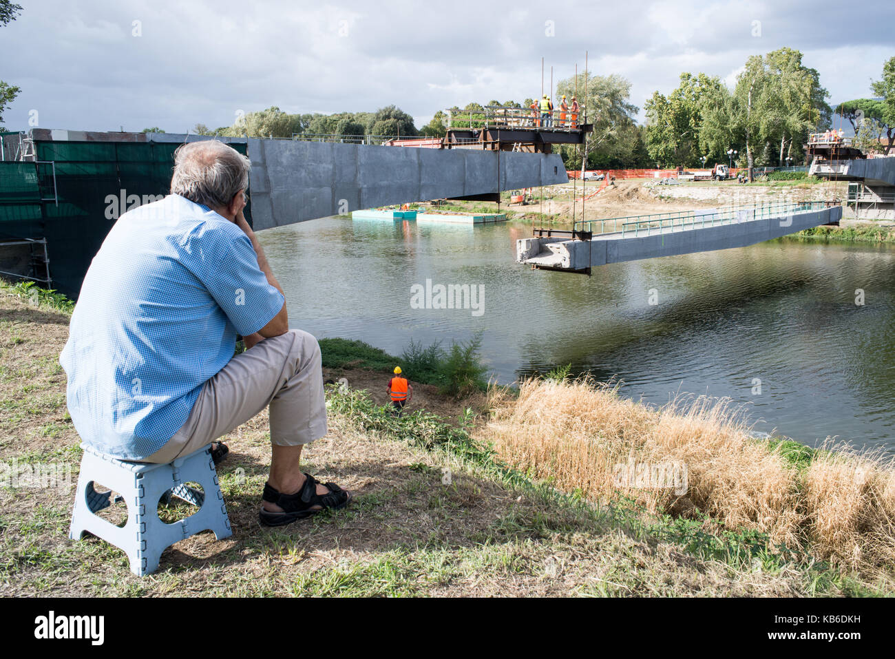 An old man looks at the renovation work of a bridge in Florence sitting on a stool Stock Photo