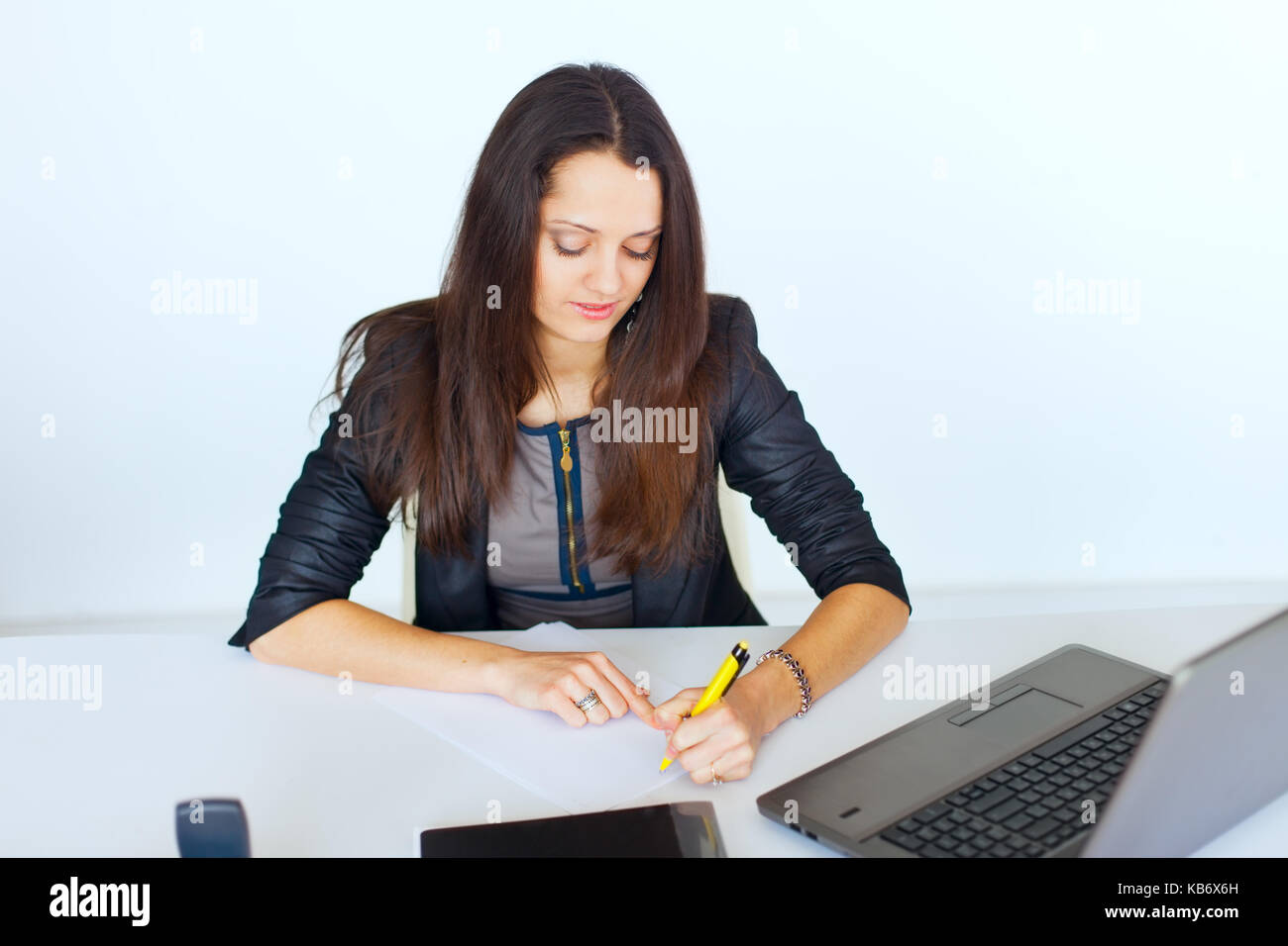 Portrait of young smiling business woman at the office desk writing ...