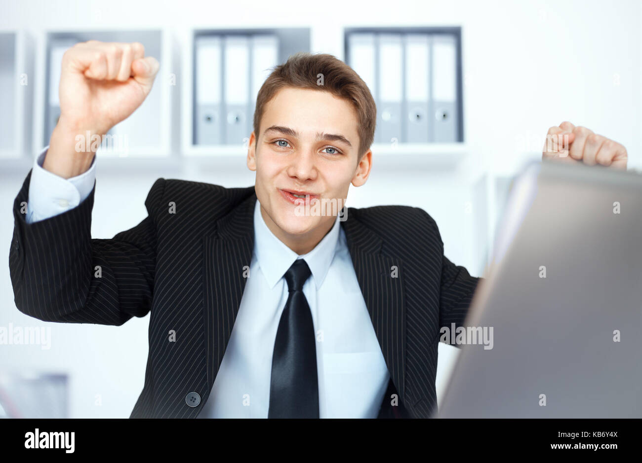 Young businessman celebrating his success with arms raised at his ...