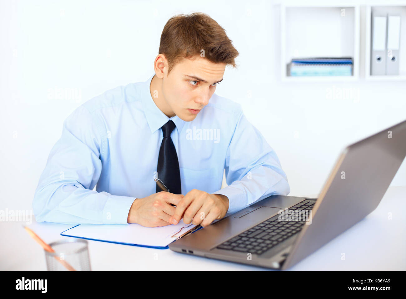 Young businessman writing on clipboard at his workplace in bright office Stock Photo