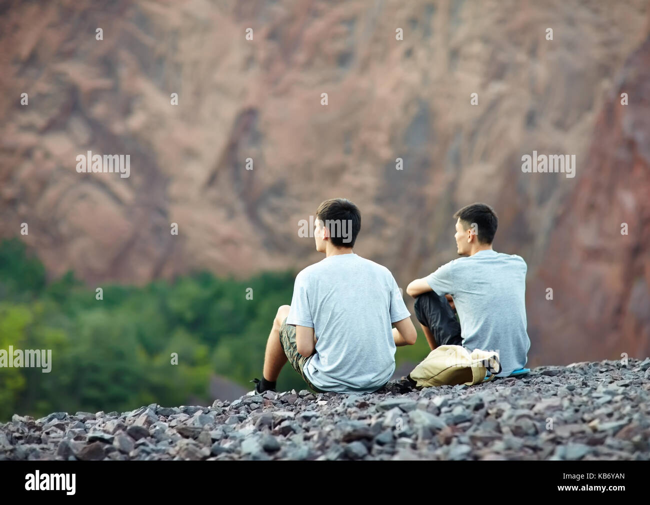 Two tourist young men sitting on rocky cliff and enjoying beautiful view Stock Photo