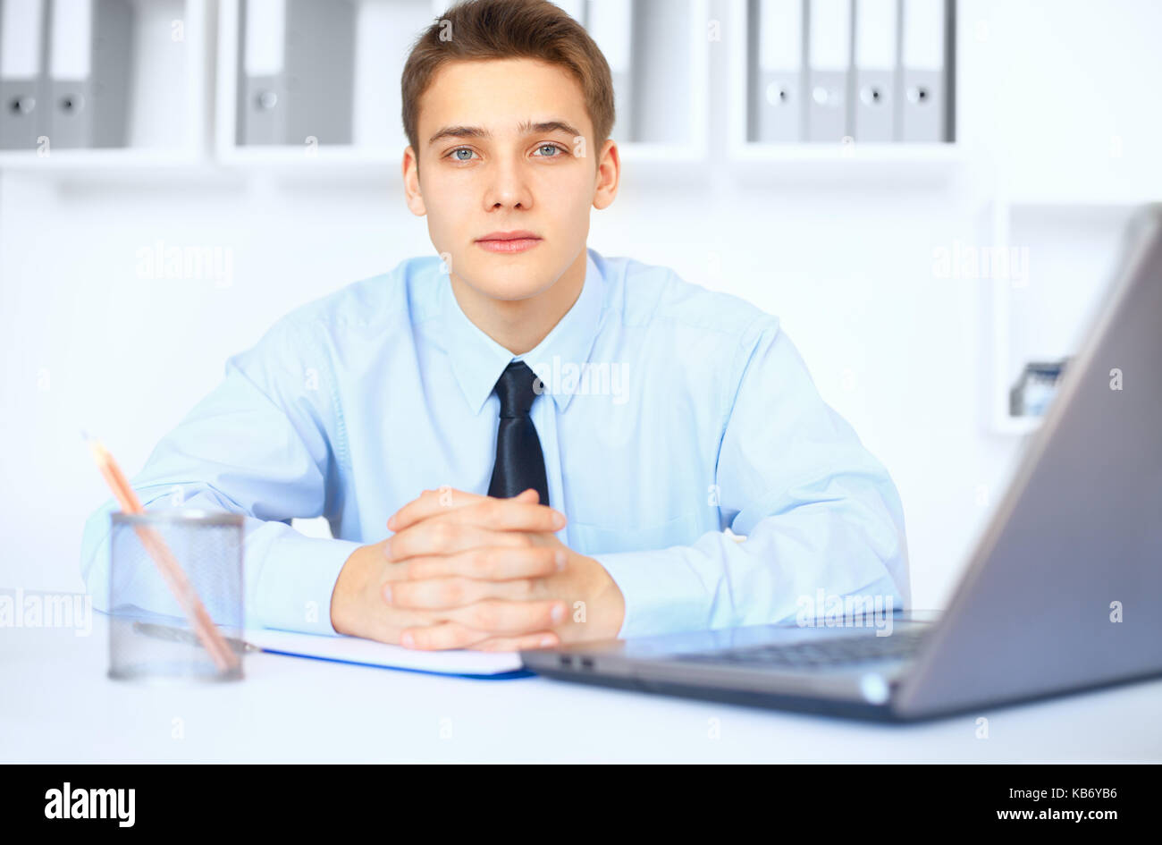 Portrait of young smiling businessman at his workplace in bright office Stock Photo