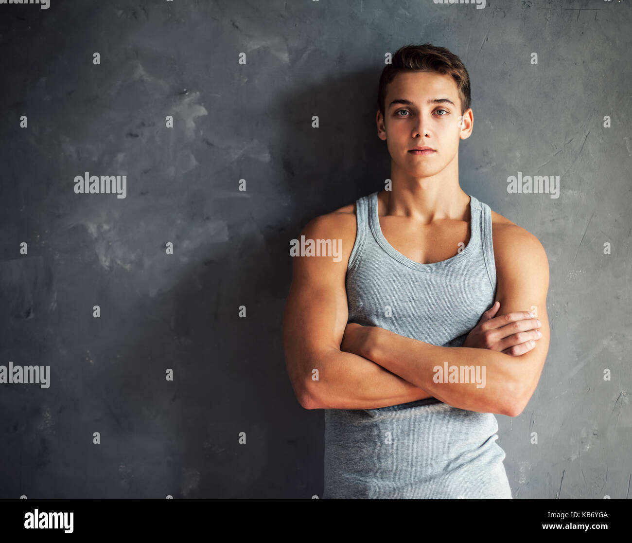 Portrait of muscular young handsome man wearing a gray undershirt against gray textured wall Stock Photo