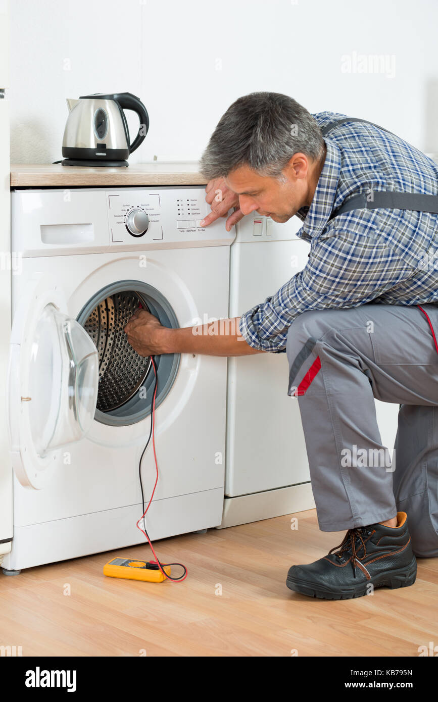 Full length of repairman checking washing machine with digital