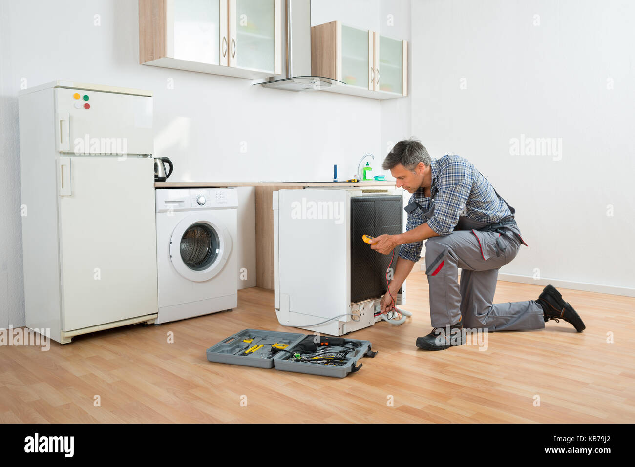 Male technician checking dishwasher with digital multimeter in kitchen