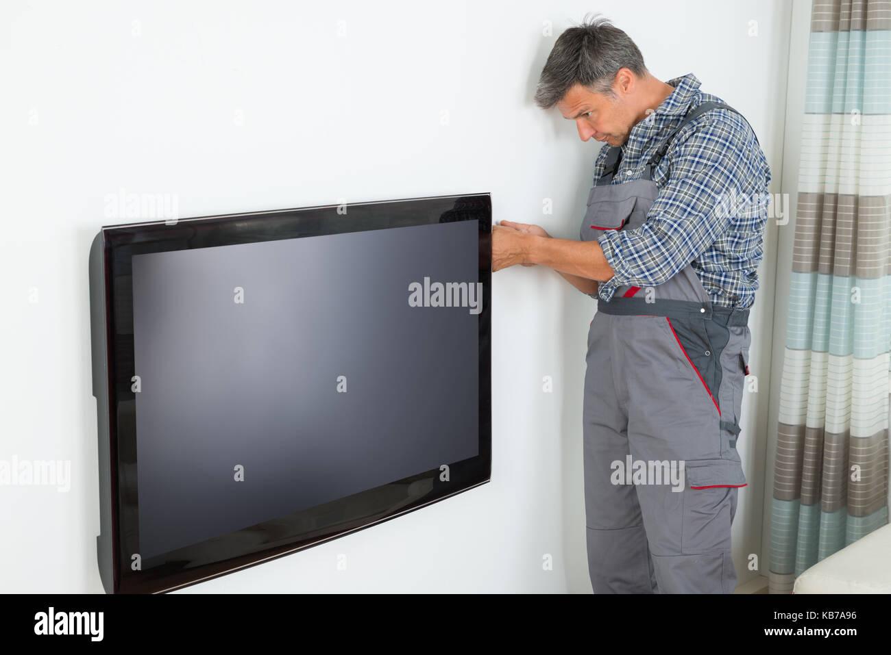 Side view of mature technician installing television at home Stock Photo