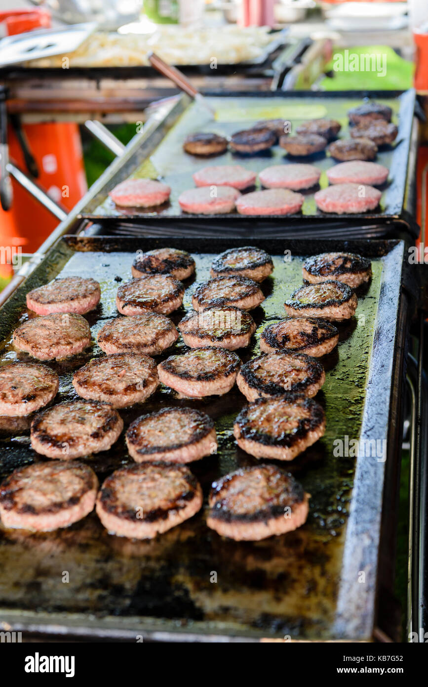 Hamburgers cooking on a hotplate griddle at an outdoor market stall. Stock Photo