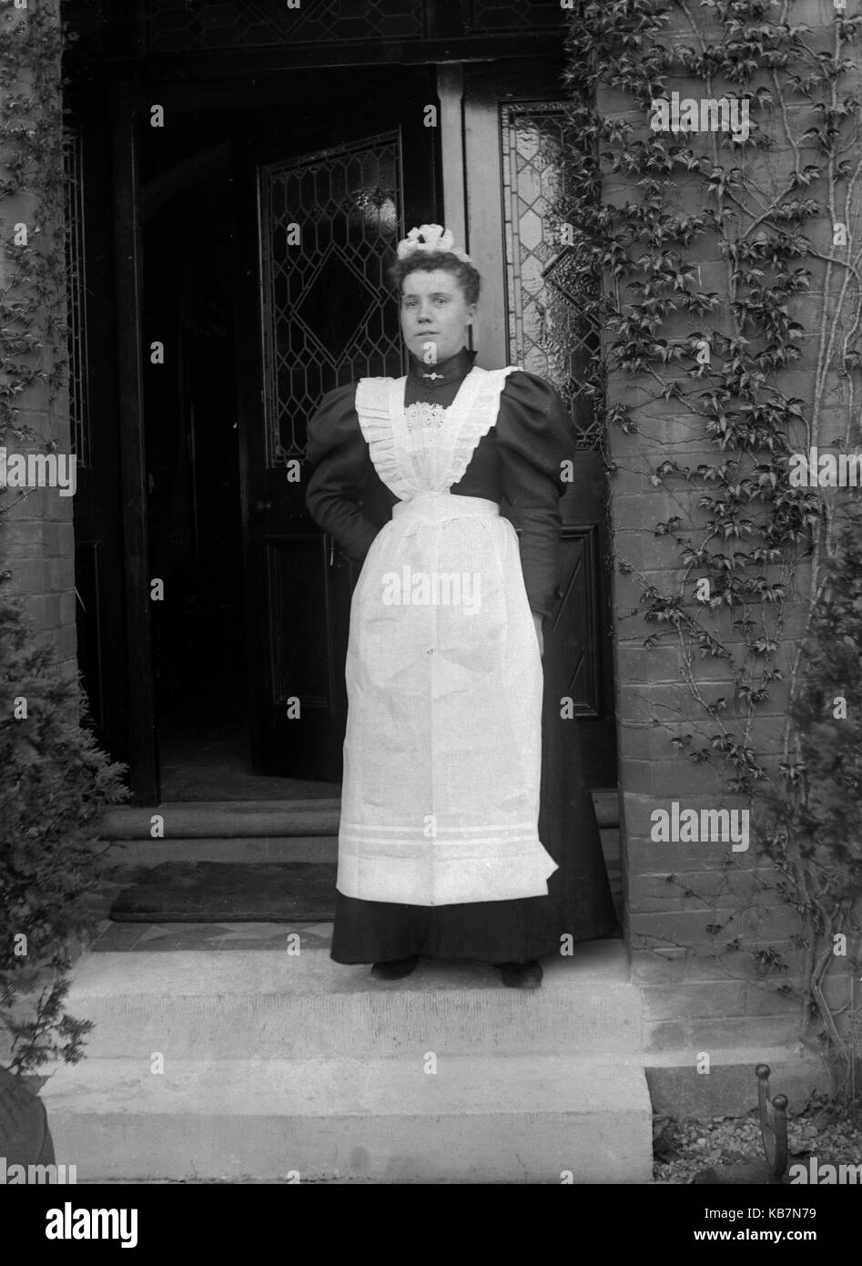 AJAXNETPHOTO. 1890 - 1914 (APPROX). LOCATION UNKNOWN. - HOUSE MAID POSING FOR CAMERA ON DOORSTEP OF HOUSE. PHOTOGRAPHER:UNKNOWN © DIGITAL IMAGE COPYRIGHT AJAX VINTAGE PICTURE LIBRARY SOURCE: AJAX VINTAGE PICTURE LIBRARY COLLECTION REF:AVL 172109 4 Stock Photo