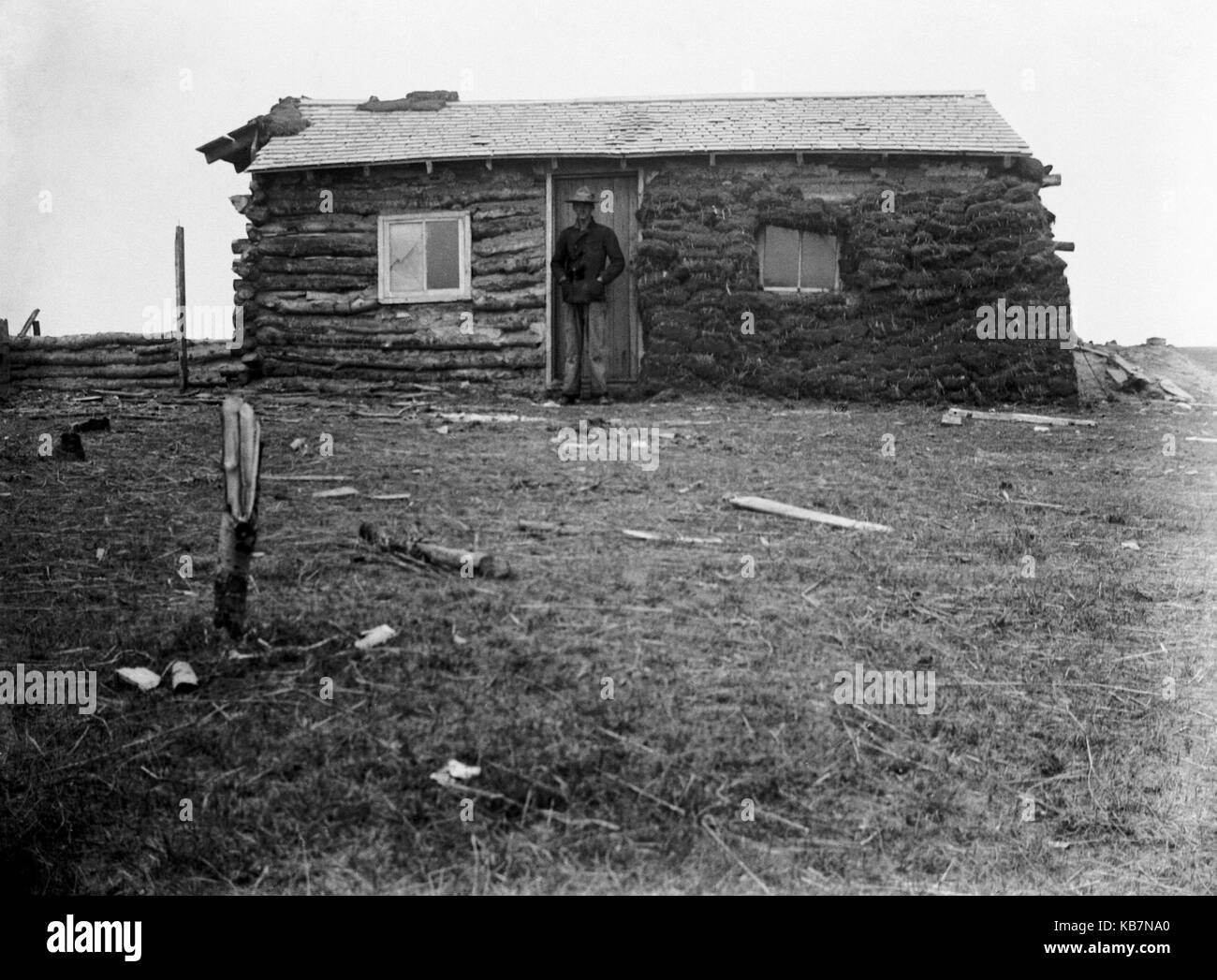 AJAXNETPHOTO. 1903. CANADA, EXACT LOCATION UNKNOWN. - ANNOTATION ON GLASS PLATE 'HAL. SHACK'. MAN IN NORTH WEST MOUNTED POLICE UNIFORM POSING OUTSIDE LOG CABIN SHACK WITH PEAT COVERING HALF FACADE.  PHOTOGRAPHER:UNKNOWN © DIGITAL IMAGE COPYRIGHT AJAX VINTAGE PICTURE LIBRARY SOURCE: AJAX VINTAGE PICTURE LIBRARY COLLECTION REF:AVL 2373 Stock Photo