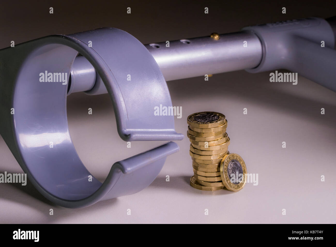 A crutch and new sterling pound coins. Concept of link between incapacity and UK pounds sterling, such as disability income and healthcare cost. Stock Photo
