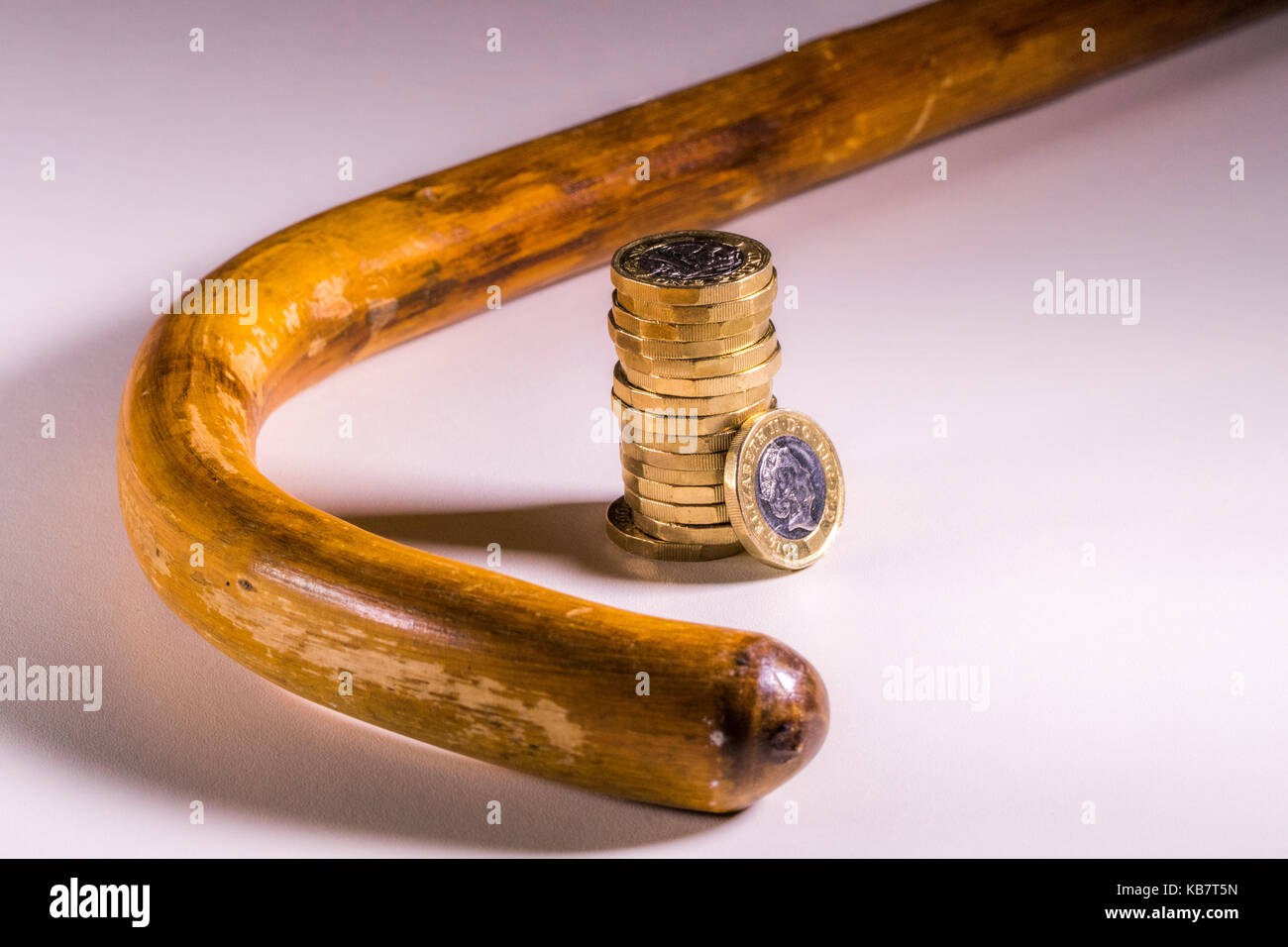 Walking stick / cane and new sterling pound coins. Concept of link between old age and UK pounds sterling, such as pension income and healthcare cost. Stock Photo