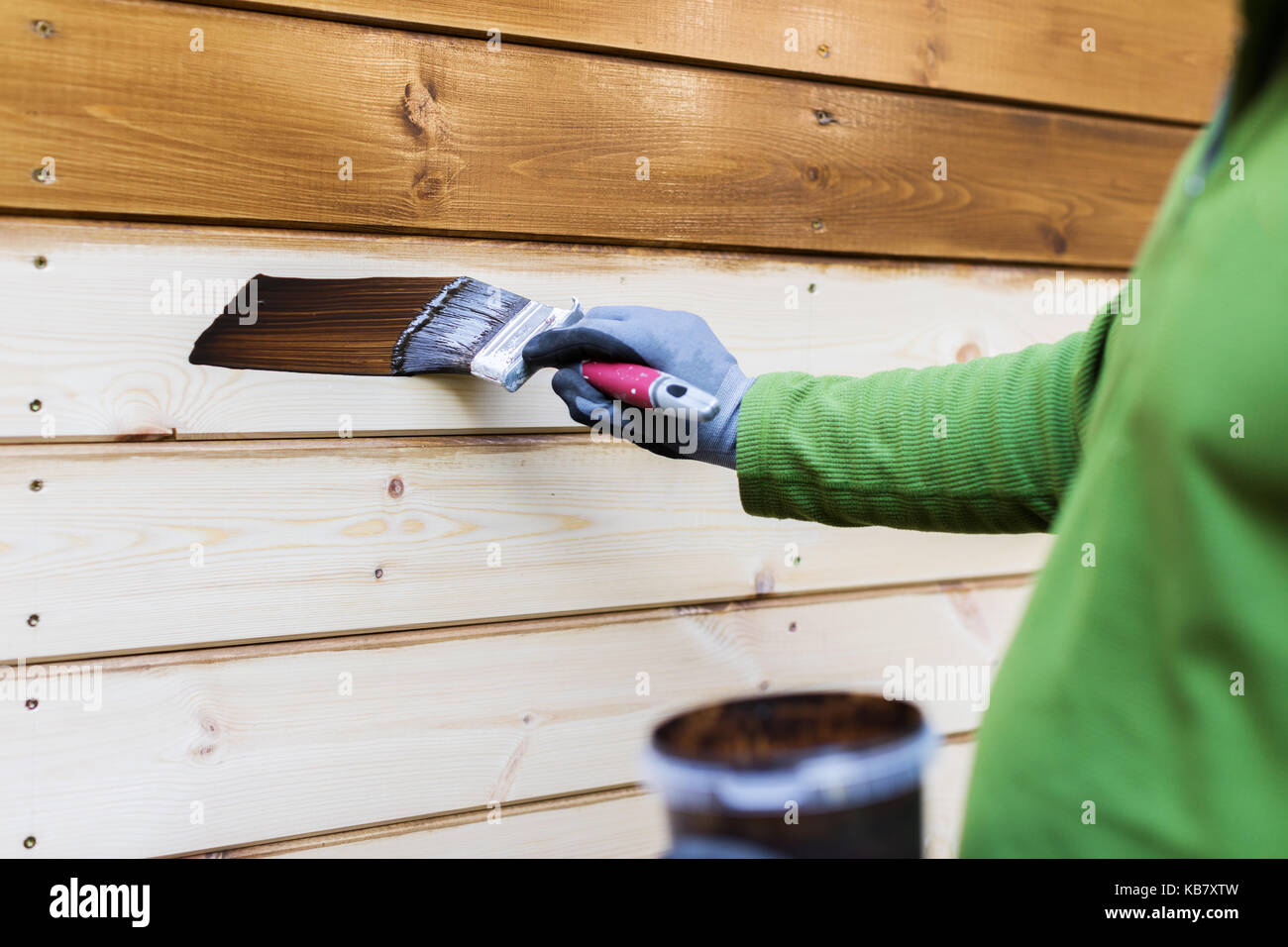 painter with paintbrush painting house facade with wood protective