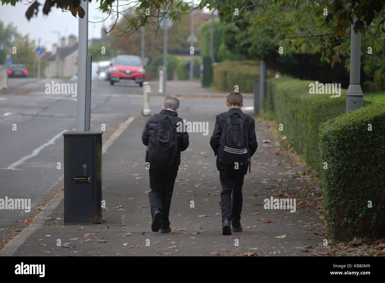 British school children boys on street messing about walking home from school together two boys car on horizon ominous Stock Photo