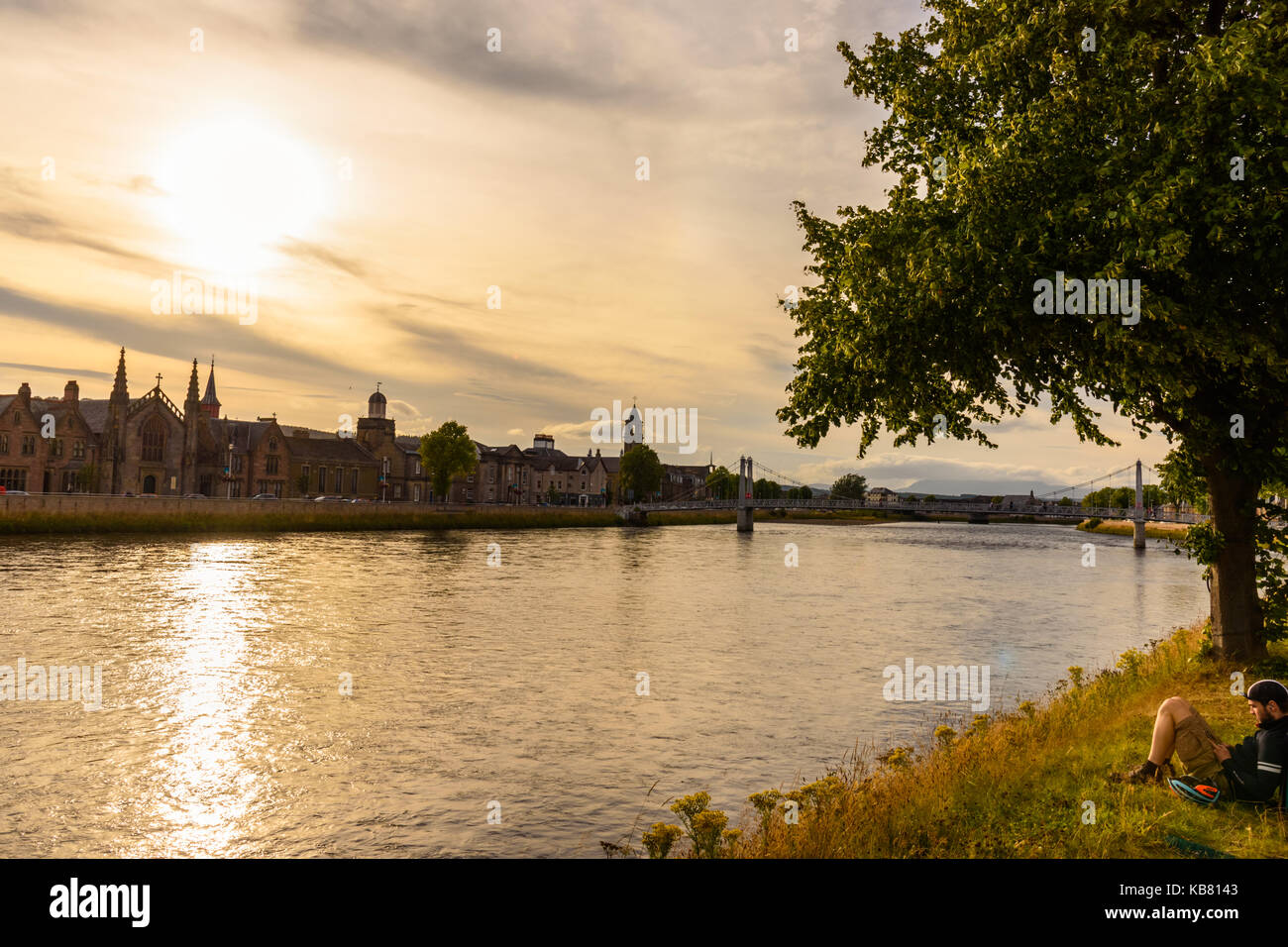 INVERNESS, SCOTLAND - AUGUST 11, 2017 - A boy relaxes on the banks of the Inverness River during sunset. Stock Photo