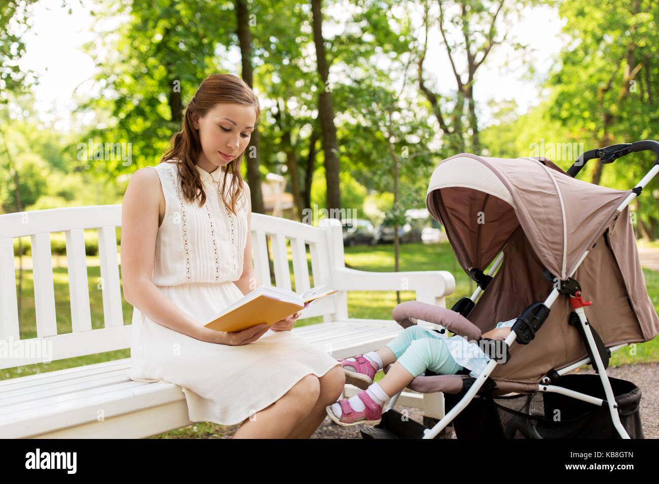 mother with child in stroller reading book at park Stock Photo