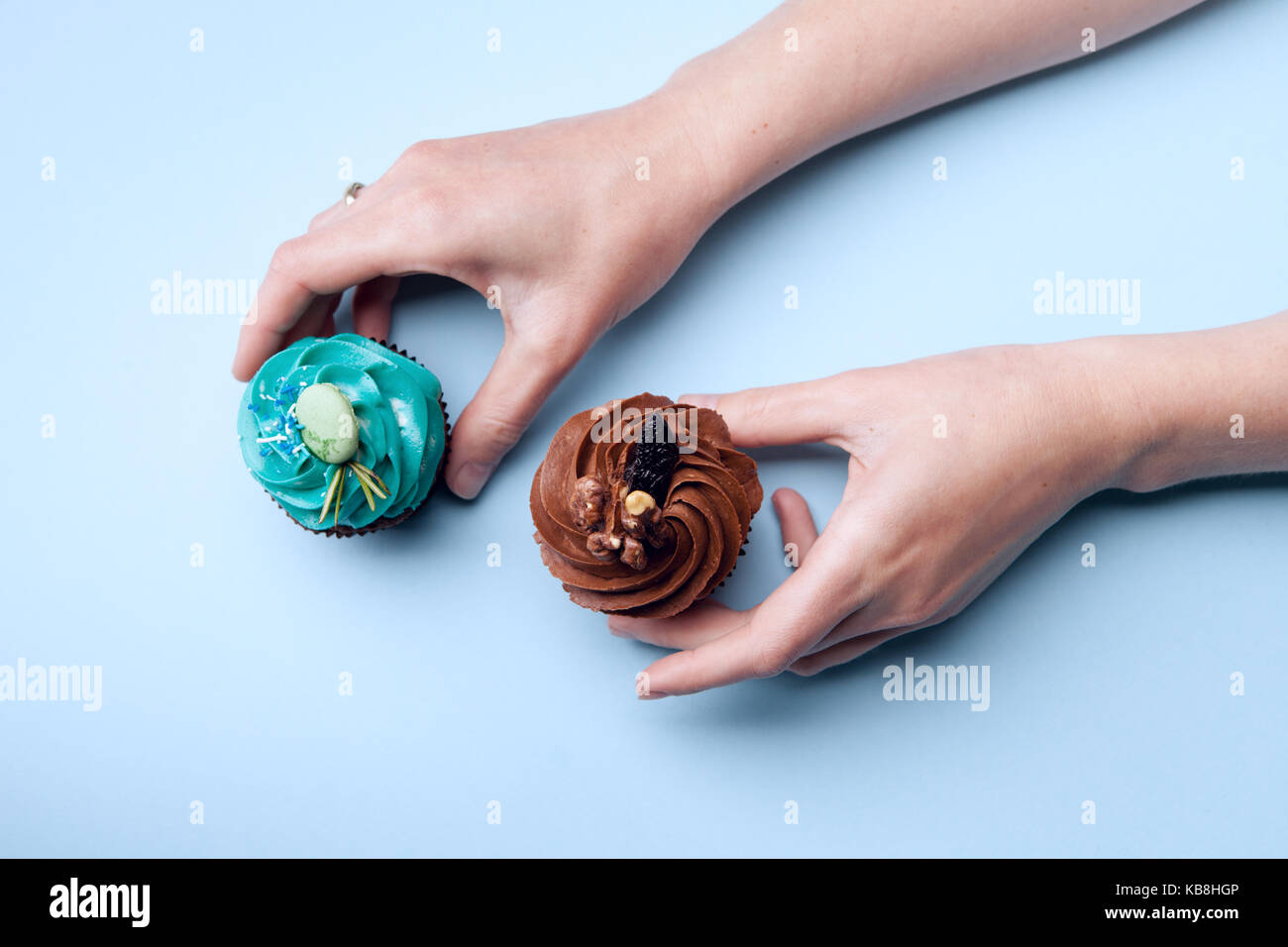 Two delicious cupcakes with cream in hands on a blue background Stock Photo